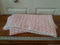 Folded pink crochet blanket on table with ruler for scale