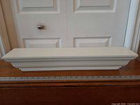 Front view of white crown molding floating shelf on table with ruler for scale