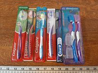 Overview of all six unopened toothbrush packages aligned on table with ruler for scale