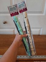 Two sealed Montoy recorders in hand, mint green and ivory with cleaning rods visible