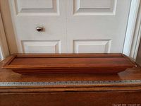 Front view of entire wooden wall shelf on table with ruler for scale