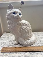 Front view of white cast iron cat door stop figurine with ruler for scale