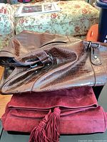 Brown croc-embossed tote stacked over burgundy suede clutch