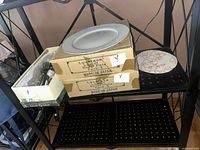Shelf with two sealed boxes marked Lovelace 6 pc Dinner Plate, loose sample plate, open carton of flatware