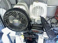Shelf with Honeywell fan, Holmes heater, additional heater, grey fan edge, GPX clock radio, power strip