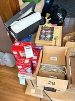 Stacked red boxes of mini and net lights beside loose coil, black box of large ornaments, gold deer figurine, box of 9 silver ornaments