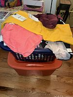 Basket with assorted clothing items on top: coral shorts, mustard dress, burgundy top, visible Nike garment