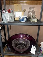 shelf view with large purple bowl, clear faceted bowl, vases, perfume bottle, ceramic jar, boxed lamp