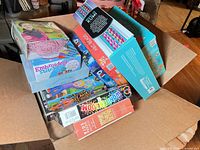 Open shipping carton showing multiple boxed craft kits, board game and puzzles
