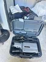 Open Panasonic hard case showing VHS-Reporter camcorder, AV cable and accessories; JVC camcorder and bag in background