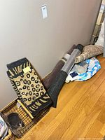 Stack of leopard print rug, rolled black mat, draft stopper, metal basket and bags
