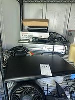 Shelf with Toshiba laptop (closed), Sylvania VCR/DVD combo, boxed portable DVD player, cables and remotes