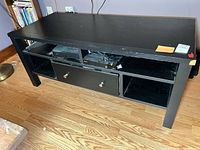 Front view of black TV stand showing open shelves and drawer