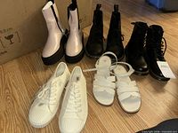 Group shot of five pairs: pink boots, two black boots, white sneakers, white sandals