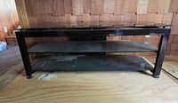 Front view of black glass TV stand showing three tiers