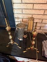 two brass andirons, pierced metal container, black cylindrical object, thermometer plaque