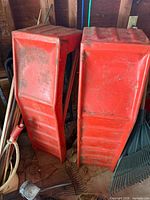 two red steel car ramps leaning against wall among garage tools