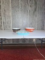 Three Pyrex pieces on table: turquoise casserole, brown bowl, orange bowl