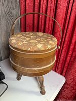 Closed wooden sewing barrel showing floral lid, handle, tripod legs