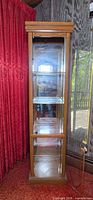 front view of tall wooden curio cabinet with glass door and shelves