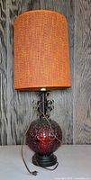 Full view of lamp showing red glass base, metal scrollwork and orange shade