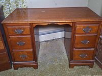 Front view of wooden desk showing six drawers, scalloped apron, bracket feet