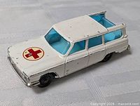 Left front view of white Husky Studebaker Red Cross wagon showing red cross decal, blue windows, overall paint condition