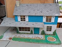 Front view of two-story blue and white tin litho dollhouse showing carport and garden