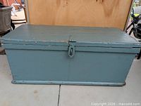 Front and top view of blue-green wooden trunk showing latch and paint wear