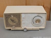 Front view showing clock, speaker grille, tuning dial, and knob