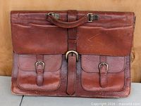 Front view showing leather briefcase, handle, two buckle pockets, central strap