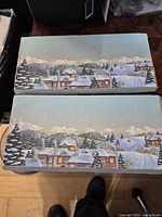 Two illustrated outer sleeves showing winter village artwork for the coin sets