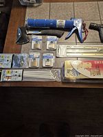 Full lot overview showing all packaged padlocks, caulking gun, axe, hose nozzle, strike rails, zip ties and screws