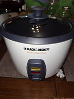 Front angled view of Black & Decker Rice Cooker Plus showing logo, warm/cook switch and glass lid