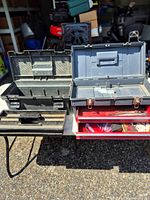 Black plastic toolbox open with insert tray and gray plastic toolbox above red trays containing abrasives