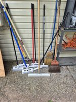 Group view of eight long-handled cleaning tools leaning against wall