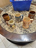 Five open-top ceramic steins on marble surface