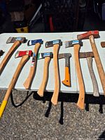Ten assorted axes, hatchets and maul laid on table