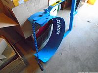 Overall view of blue Morse drum lifter showing clamp plate, chain and semi-circular cradle