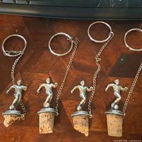 Four metal soccer player bottle stoppers laid out showing overall form, corks and key rings