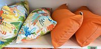 Two tropical floral and two solid orange cushions displayed on shelf
