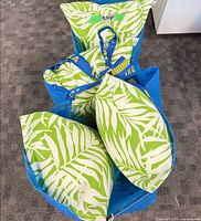 Four green and white palm print lumbar cushions inside blue bag