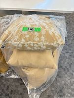 Four cushions stacked in plastic packaging showing solid tan and patterned tan/white covers