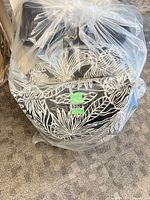 Four stacked black cushions with white tropical pattern sealed in clear plastic
