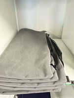 Stack of four grey Sunbrella cushion covers with black zippers folded on shelf