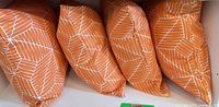 Four orange geometric patterned square cushions side by side