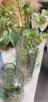 Two textured glass vases with faux eucalyptus stems on tabletop