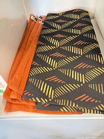 Stack of four orange covers and one folded black patterned cover on shelf
