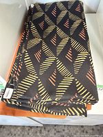 Stack of cushion covers showing black patterned and solid orange covers