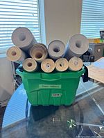 Front view of green tote containing approximately 10 wallpaper rolls of varying diameters